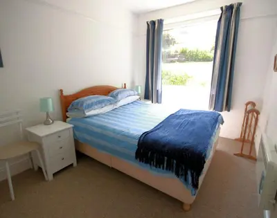 a bedroom with a bed with a blue blanket and a window at Gullsway Sandpiper in Polzeath
