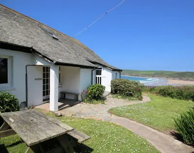 a white house with a picnic table and the beach at Gullsway Sandpiper in Polzeath