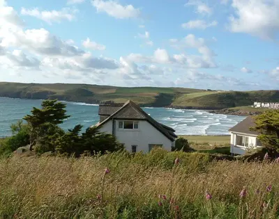 a house on a hill next to a body of water at Gullsway September Tide in Polzeath