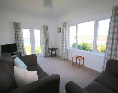 a living room with a couch and two windows at Gullsway September Tide in Polzeath