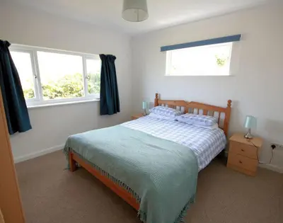 a bedroom with a bed and two windows at Gullsway September Tide in Polzeath