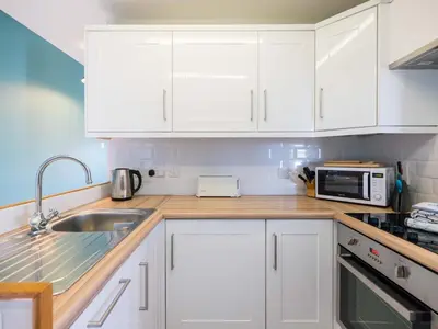 a kitchen with white cabinets and a sink and a microwave at Pinewood Flat 5 in Polzeath