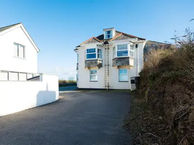 a white house on a hill next to a driveway at Pinewood Flat 5 in Polzeath