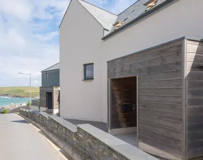 a white house with a wooden garage on the side of it at Rainer Rocks in Polzeath