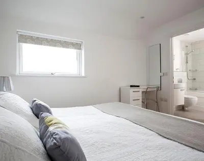 a white bedroom with a bed and a window at The Beach Hut in Polzeath