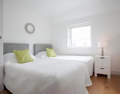 two white beds in a white room with a window at The Beach Hut in Polzeath