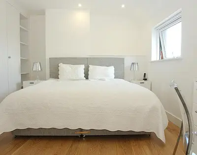 a white bedroom with a large bed with two lamps at The Beach Hut in Polzeath