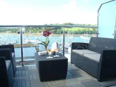 a balcony with chairs and a table with a view of a harbor at Topsail - Falmouth in Falmouth