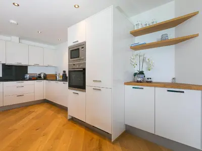 a white kitchen with white cabinets and a wooden floor at Crystal Bay in St Ives