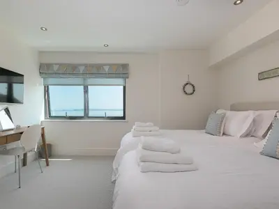a white bedroom with a bed and a desk and a window at Crystal Bay in St Ives