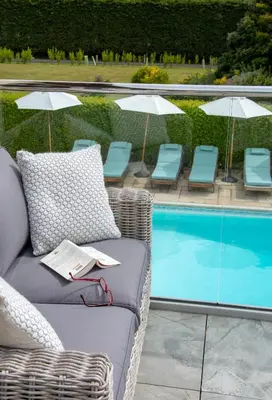 a wicker chair sitting next to a swimming pool at Hewas Water House - Private Pool, Hot Tub & Games Room in Grampound