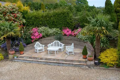 a patio with two chairs and flowers and plants at Hewas Water House - Private Pool, Hot Tub & Games Room in Grampound