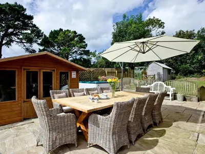 a wooden table with chairs and an umbrella at Hewas Water House - Private Pool, Hot Tub & Games Room in Grampound