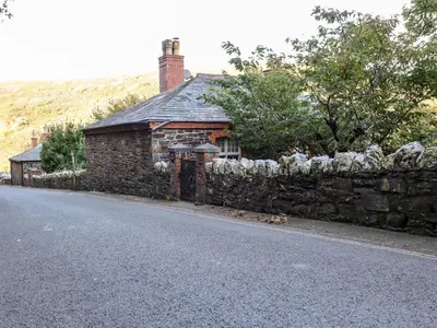 a stone house with a stone wall next to a street at Lewarne in Boscastle