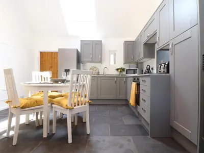 a kitchen with white cabinets and a table and chairs at The Dairy in Helston