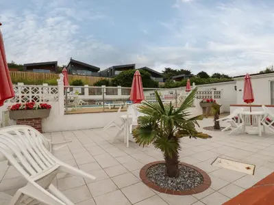 a patio with white chairs and red umbrellas at 7 Europa Court in Newquay
