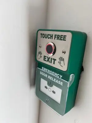 a green emergency door release sign on a wall at Apartment No 8 - Stay in style in the heart of the Cathedral City. in Truro