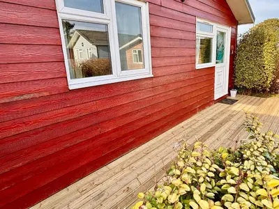 a red house with a window and a wooden deck at Trevone - Chalet 130 in Padstow