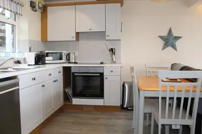 a kitchen with white cabinets and a table with a microwave at Lobster Pot - Mount Brioni in Downderry