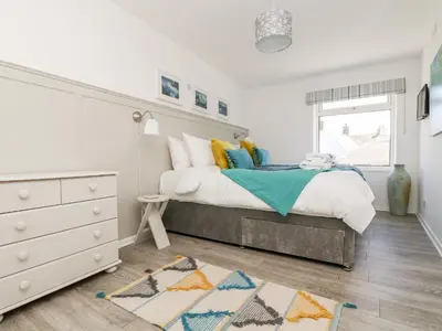 a white bedroom with a bed and a dresser at Rock Pool House in Helston
