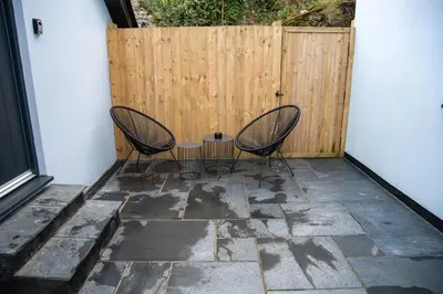 two chairs and a table on a patio with a fence at Valley View Studio Annexe in Downderry