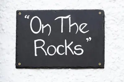 a black sign with the words on the rocks at Modern House in Looe, Near Beach and Bars with Great Views and free access to a nearby Indoor Swimming Pool in Looe
