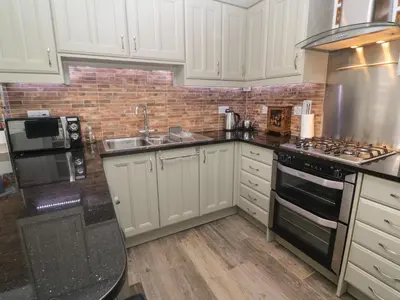 a kitchen with white cabinets and a brick wall at Primrose Cottage in Hayle