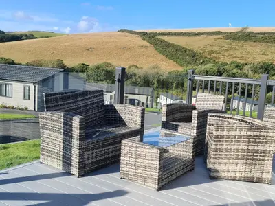 a patio with chairs and a glass table on a deck at Mawgan Pads Mawgan Porth in Mawgan Porth