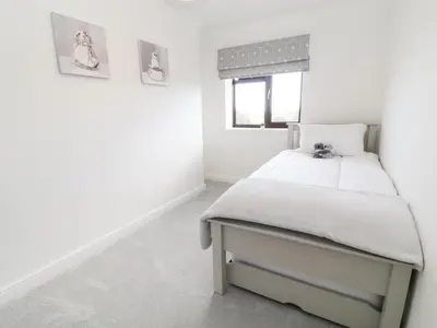 a white bedroom with a bed and a window at 12 Claremont Falls in Looe