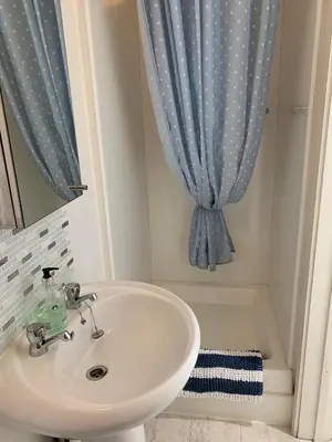 a bathroom with a sink and a blue shower curtain at Little Karenza is the perfect Cornish getaway in Saint Anthony