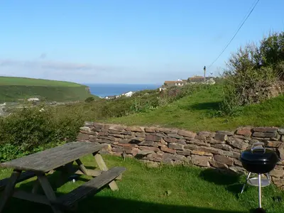 a picnic table and a grill next to a stone wall at Porth Farm Annexe in Newquay