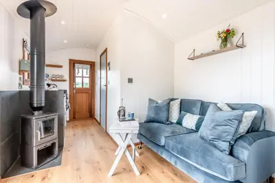 a living room with a blue couch and a wood stove at Daisy Park Shepherds Hut in Looe
