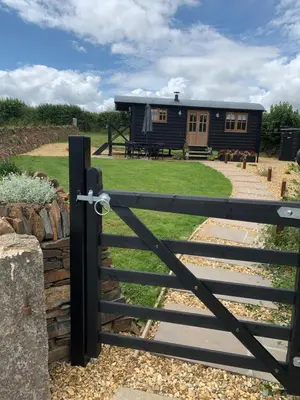 a gate to a black cabin with a fence at Daisy Park Shepherds Hut in Looe