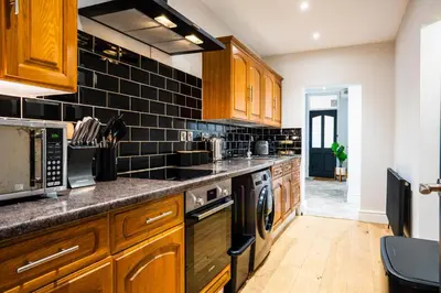 a kitchen with wooden cabinets and black tiles on the wall at Central, stylish 3 bed apartment with sea views in Newquay