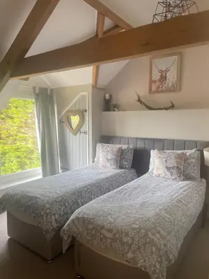 a bedroom with two beds and a window at The Barn at Well Cottage in Bude