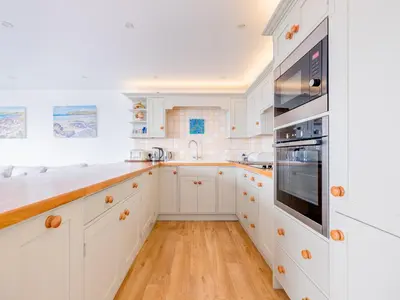 a white kitchen with wooden floors and white cabinets at Slipway 21 in Padstow