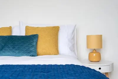 a bed with blue and yellow pillows and a lamp at Bells Chapel - Bright Rooftop Apartment in the Centre of Town with Juliet Balconies in Falmouth