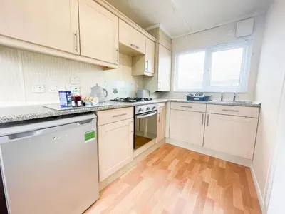 a kitchen with white cabinets and a wooden floor at Stowaway St Merryn in St Merryn