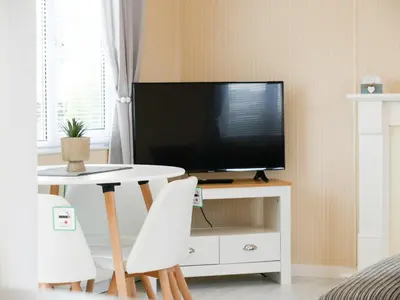a living room with a tv and a table with white chairs at Stowaway St Merryn in St Merryn