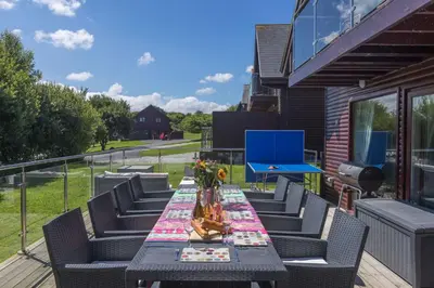 a table on a deck with chairs and a blue table at Lodge 27 - Resort & Spa - Parking - Private Hot Tub in Saint Columb Major