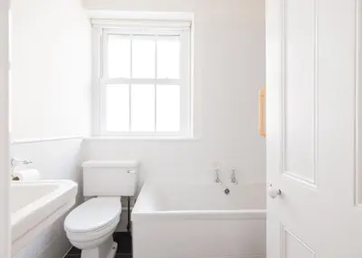a white bathroom with a toilet and a tub and a window at The Terrace 2 in Padstow