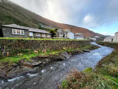a stone wall next to a river next to a house at Olde Carpenters Cottage in Boscastle