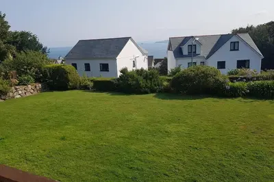 a white house and a yard with a grass field at St Ives apartment private parking with garden 10 minute walk into town and beach in St Ives