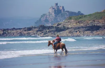 a man riding a horse on the beach with a castle in the background at Little Chyryn Perranuthnoe in Perranuthnoe