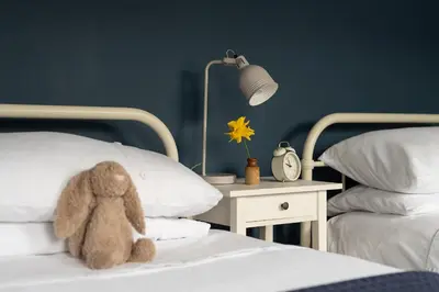a teddy bear sitting on a bed next to a night stand at Swallow Cottage in Port Isaac
