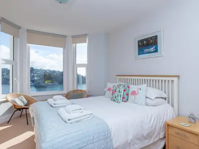 a bedroom with a bed and two chairs and windows at Apartment 2 The Wheelhouse in Fowey