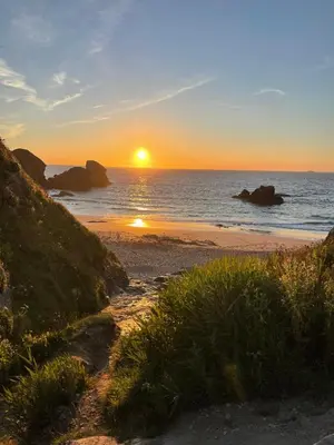 a sunset on a beach with the ocean and rocks at Sunny Corner, Padstow. Spacious 3 bedrooms, 2.5 bathrooms, parking, garden. in Padstow