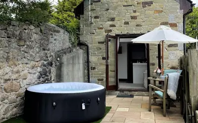 a bath tub sitting next to a stone building with an umbrella at The Stables - Detached Cottage with Private Garden & Hot Tub in St Austell