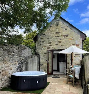 a bath tub in front of a stone building at The Stables - Detached Cottage with Private Garden & Hot Tub in St Austell