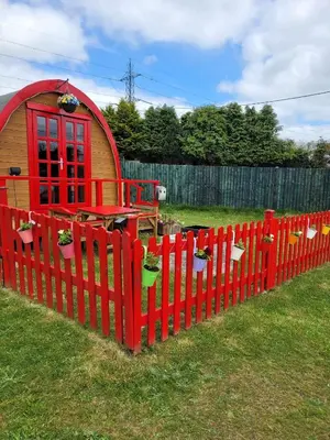 a red fence with a small house in a yard at Cozy Cabin Retreat in Saint Austell in Lanivet